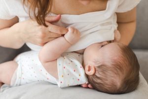 A young mother is breastfeeding her baby in a cafe while she is having a tea time