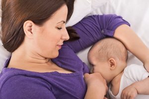 Smiling happy beautiful mother breastfeeding her baby infant