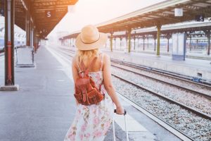 summer travel, woman with suitcase waiting for her train on platform of railway station